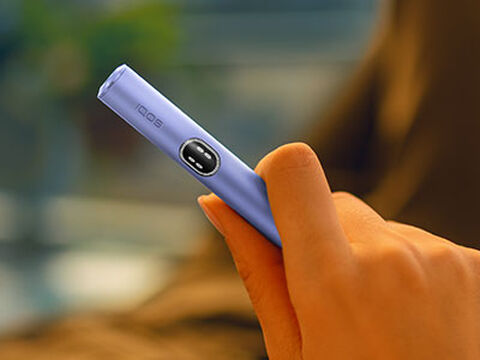 A woman holding an IQOS device looking at a laptop.
