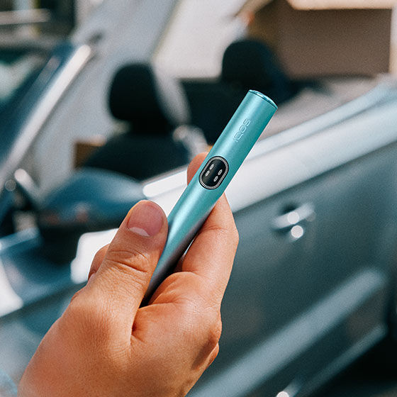 An IQOS ILUMA device in a charging station with a Pocket Charger on a table.
