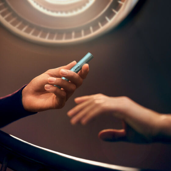 Koyu merdivenli arka plan - IQOS cihazı tutan eller - IQOS logosuyla birlikte