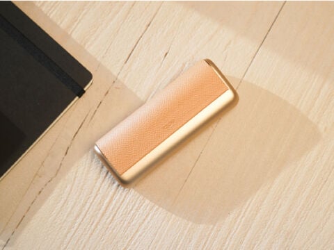A woman holding an IQOS device looking at a laptop.
