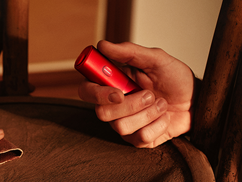 Hands holding smartphones and one IQOS device.