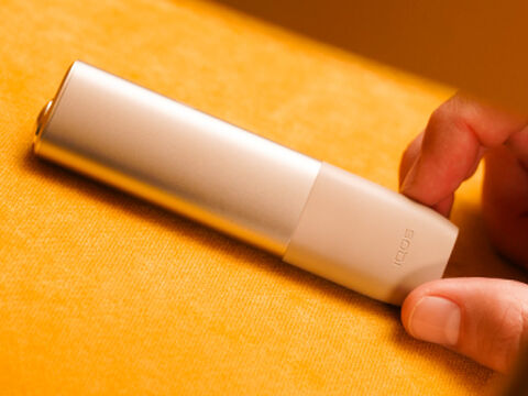 Hands holding smartphones and one IQOS device.