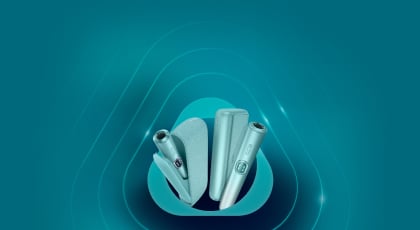 Promotional banner for IQOS ILUMA Prime featuring a sleek black device and charging case on a turquoise background. The text announces a new reduced price of 28 KWD, down from the original 35 KWD, with a note about the recommended retail price.